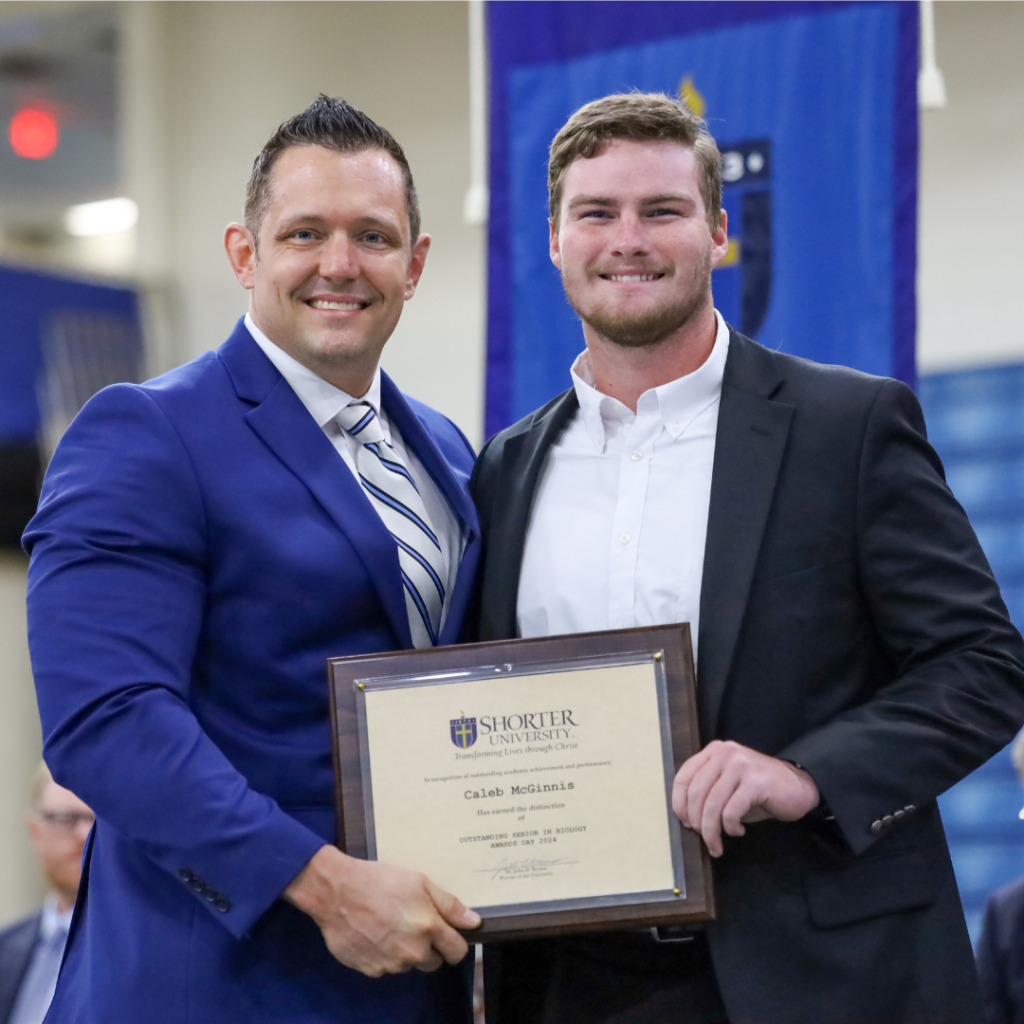 Dr. Clint Helms and Caleb McGinnis standing with the award.
